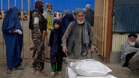 A Taliban fighter stands guard as people receive food rations distributed by a humanitarian aid group in Kabul in May 2022. 