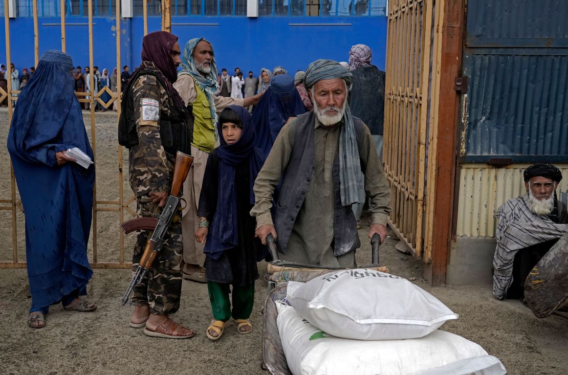 A Taliban fighter stands guard as people receive food rations distributed by a humanitarian aid group in Kabul in May 2022. 