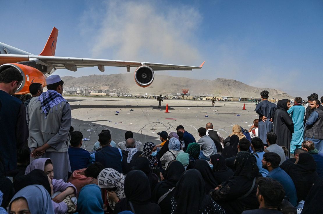 Afghan people sit as they wait to leave the Kabul airport in Kabul on August 16, 2021, after a stunningly swift end to Afghanistan's 20-year war. 
