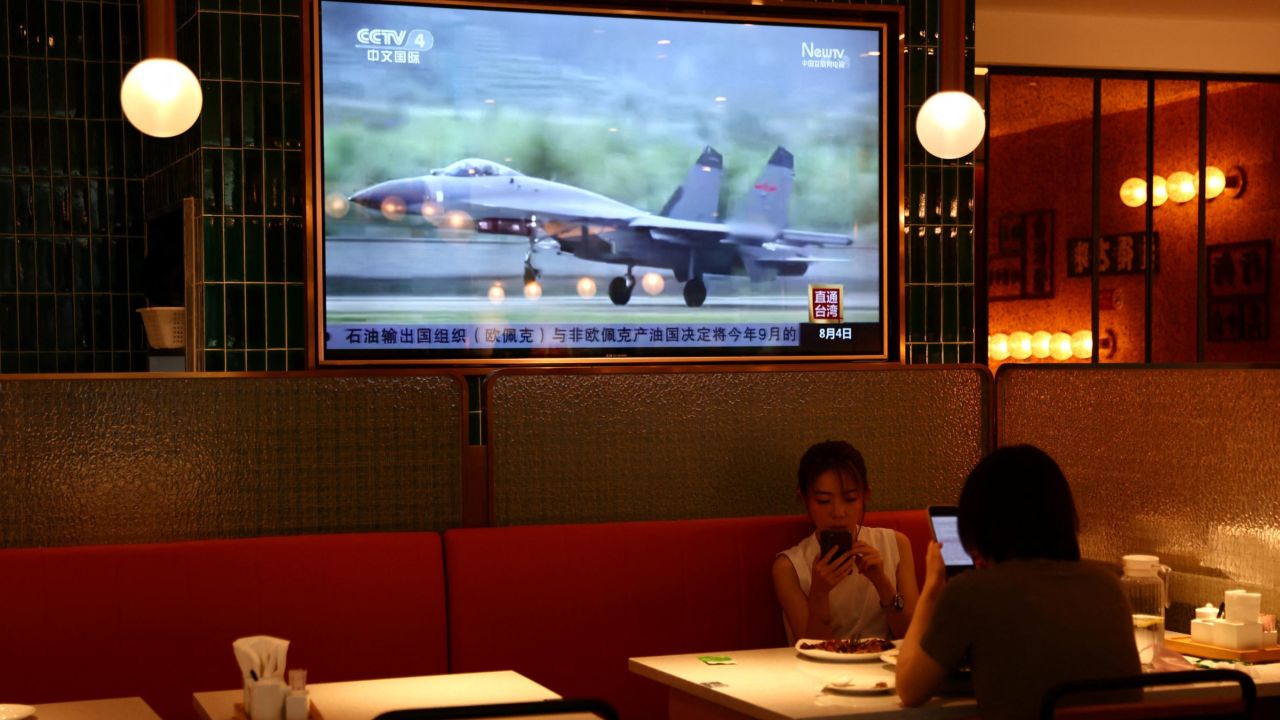 People dine at a restaurant in Beijing near a screen showing news footage of military exercises near Taiwan, August 5, 2022.