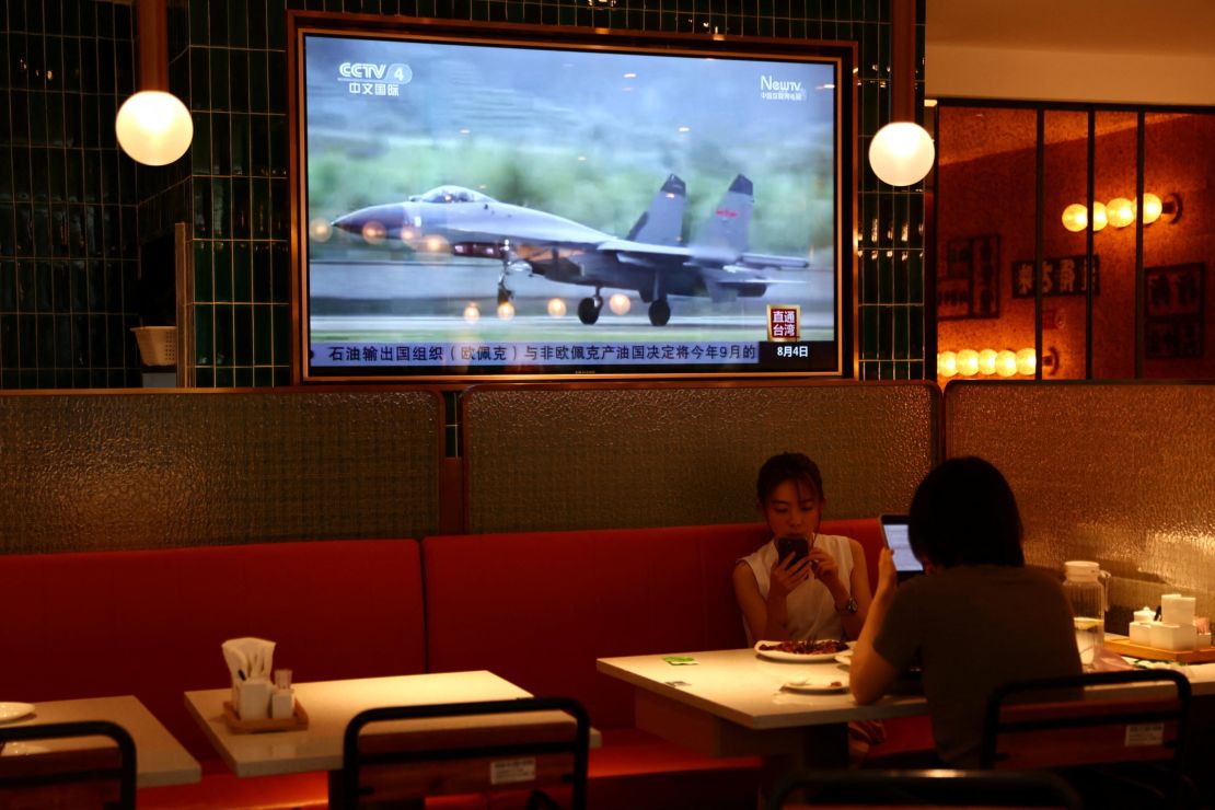 People dine at a restaurant in Beijing near a screen showing news footage of military exercises near Taiwan, August 5, 2022. 