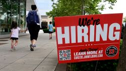 People walk past a "now hiring" sign posted outside of a restaurant in Arlington, Virginia on June 3, 2022.