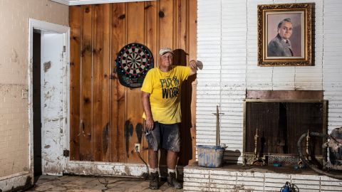 Sam Quillen poses for a portrait next to a painting of his father at his damaged property, which was a dentist's office as well as residential housing.