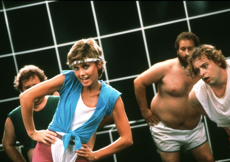 Newton-John in a classic headband and high-waisted leotard combo while filming the music video for her seminal 1981 hit "Physical."
