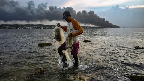 A man fishes as smoke rises from the massive fire at a fuel depot in Matanzas, Cuba, on August 9, 2022.