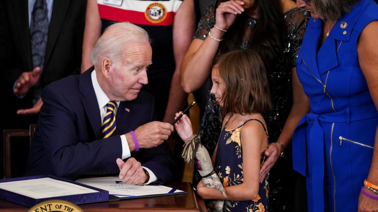 U.S. President Joe Biden hands a pen to Brielle Robinson, the daughter of Sgt. 1st Class Heath Robinson, as her mother, Danielle Robinson, stands by during a signing ceremony for "the Sergeant First Class Heath Robinson Honoring our Promises to Address Comprehensive Toxics (PACT) Act of 2022," in the East Room of the White House in Washington, U.S., August 10, 2022. REUTERS/Kevin Lamarque