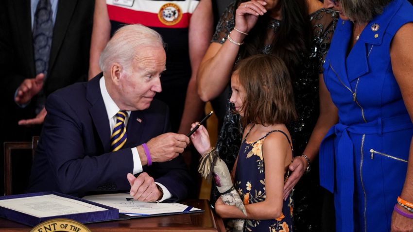 U.S. President Joe Biden hands a pen to Brielle Robinson, the daughter of Sgt. 1st Class Heath Robinson, as her mother, Danielle Robinson, stands by during a signing ceremony for "the Sergeant First Class Heath Robinson Honoring our Promises to Address Comprehensive Toxics (PACT) Act of 2022," in the East Room of the White House in Washington, U.S., August 10, 2022. REUTERS/Kevin Lamarque