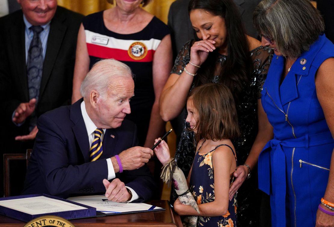 U.S. President Joe Biden hands a pen to Brielle Robinson, the daughter of Sgt. 1st Class Heath Robinson, as her mother, Danielle Robinson, stands by during a signing ceremony for "the Sergeant First Class Heath Robinson Honoring our Promises to Address Comprehensive Toxics (PACT) Act of 2022," in the East Room of the White House in Washington, U.S., August 10, 2022. REUTERS/Kevin Lamarque