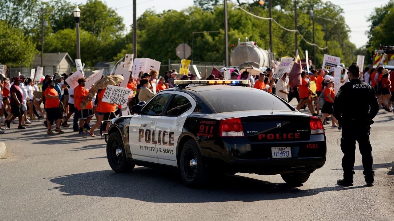 A Uvalde police officer watches as family and friends of those killed and injured in the school shootings at Robb Elementary take part in a protest march and rally, Sunday, July 10, 2022, in Uvalde, Texas. Families and residents are seeking answers and changes after the tragedy. (AP Photo/Eric Gay)