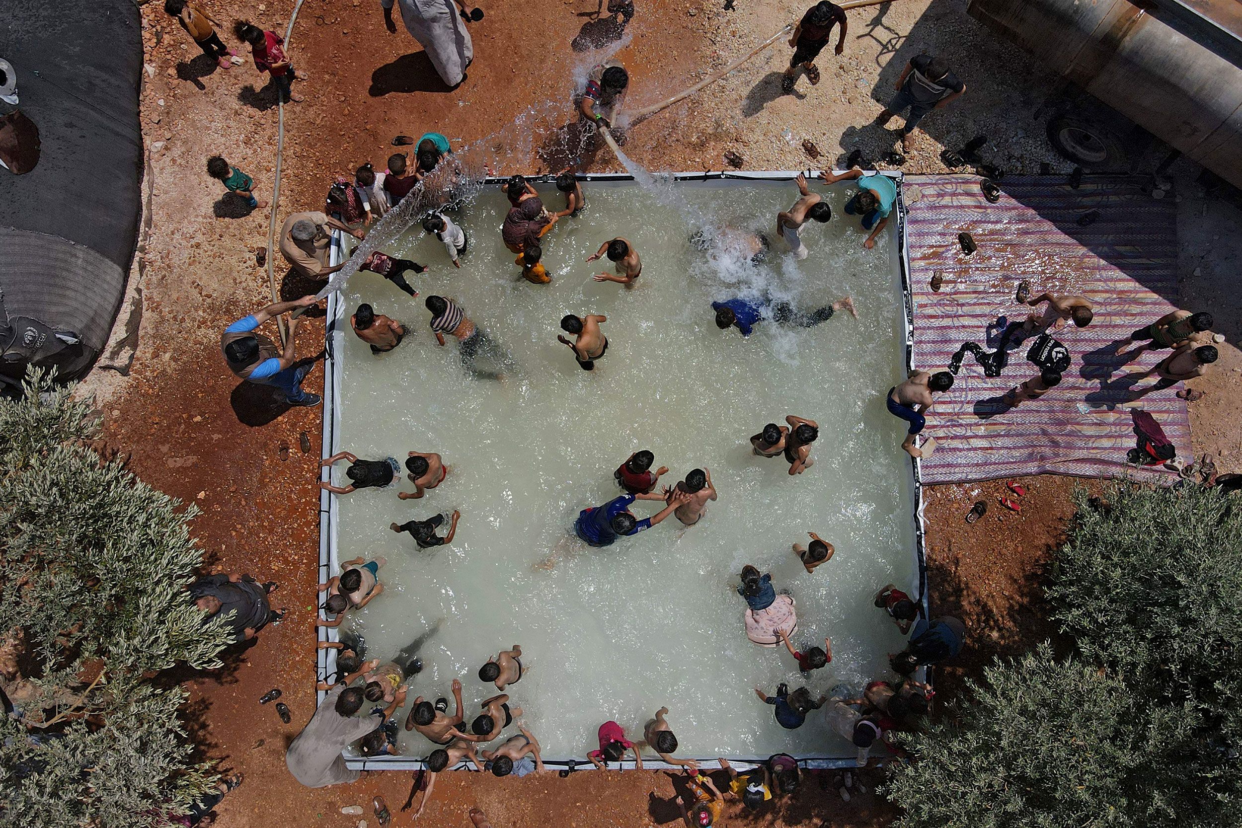 Children play in a portable swimming pool at a camp for displaced people in Kafr Yahmul, Syria.