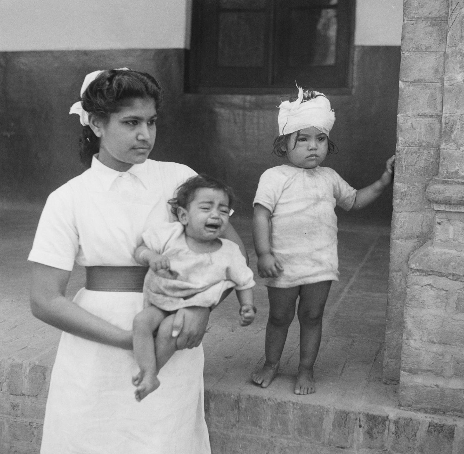 A nurse holds a crying orphaned child, as she stands beside her wounded sibling, following communal violence in Amritsar, Punjab. The children's mother was stabbed to death in March 1947 during communal riots in the months leading up to Partition.