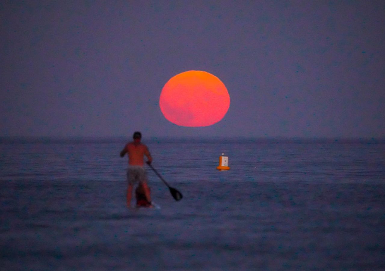 A paddle boarder watches the rising sturgeon moon off Swanpool Beach on August 11 in Falmouth, England.