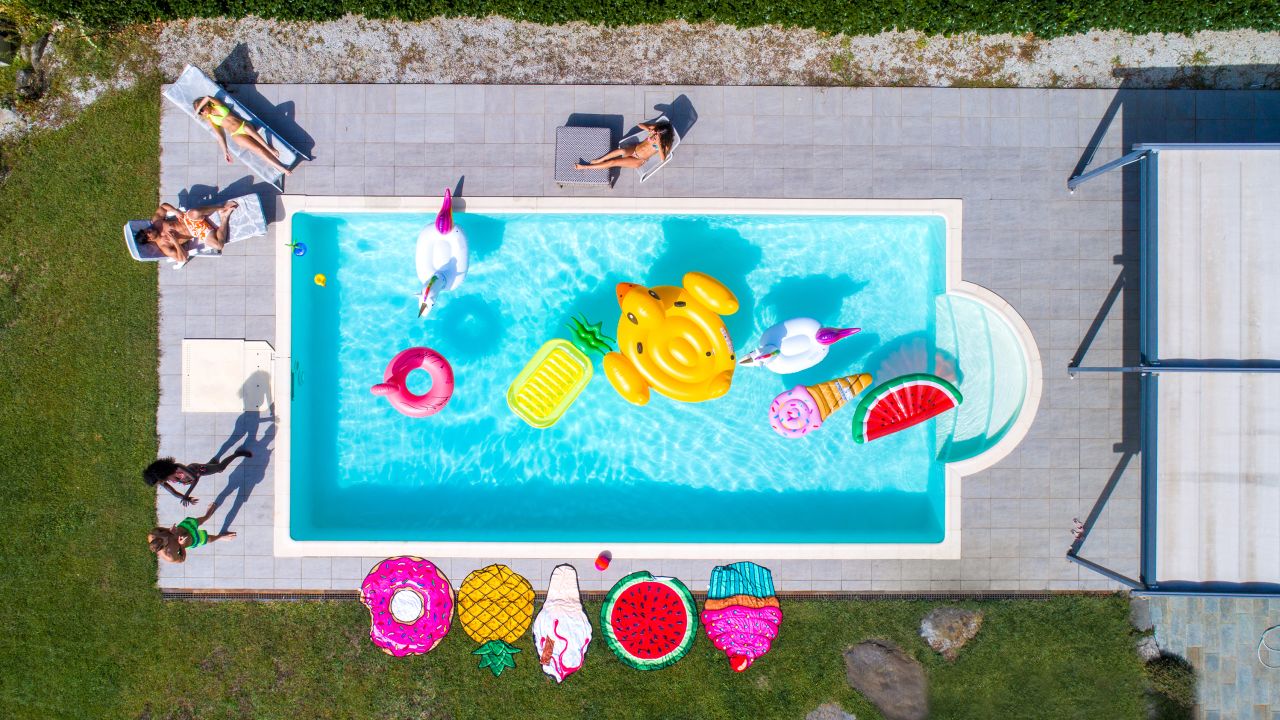 Happy people partying in an exclusive swimming pool with animal and fruit shapes mats, view from above