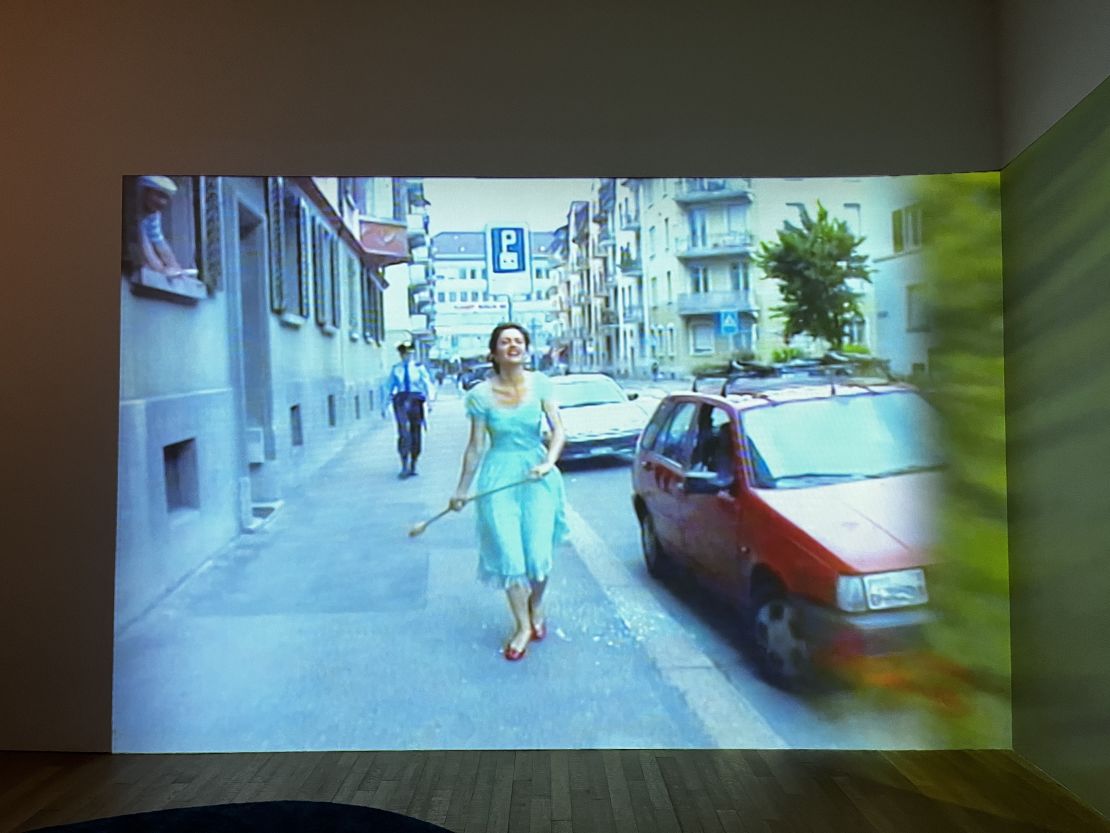 "Ever is Over All" (1997) is a two-channel video: one side shows fields of flowers, while the other (pictured) shows Rist skipping down a car-lined street, flower in hand. 