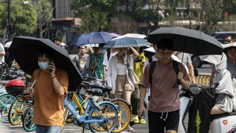 Office workers carrying umbrellas to shield from the sun walk in Hangzhou, China, on Tuesday, Aug. 2, 2022. 