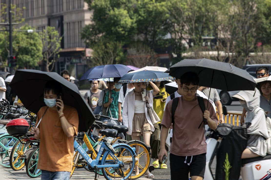Office workers carrying umbrellas to shield from the sun walk in Hangzhou, China, on Tuesday, Aug. 2, 2022. 