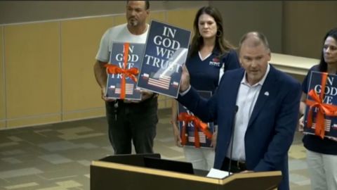 A Christian wireless provider has donated framed posters of the motto "In God We Trust," seen here at a meeting of suburban Dallas school district, which will be obliged by a new state law to display them.
