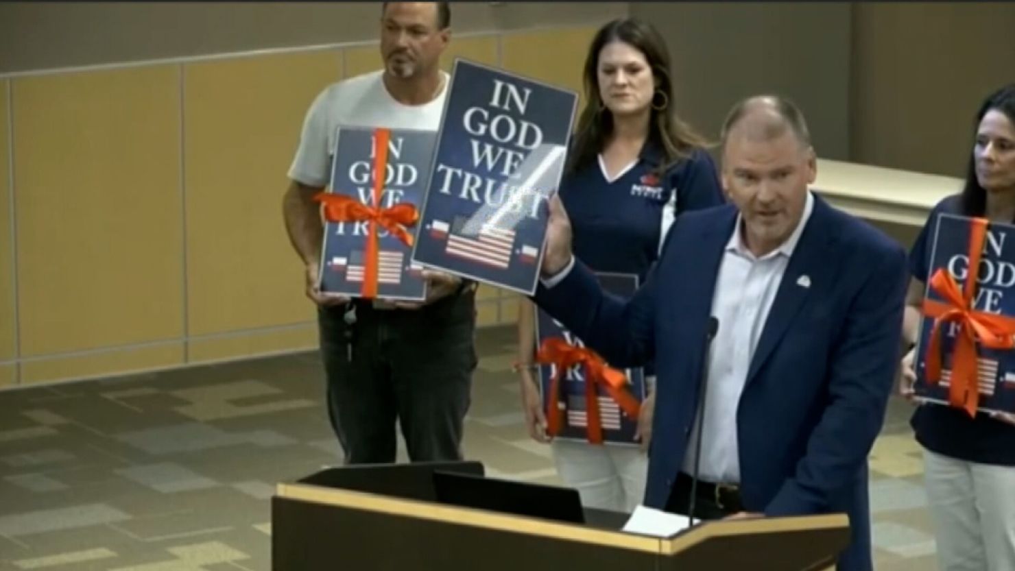 A Christian wireless provider has donated framed posters of the motto "In God We Trust," seen here at a meeting of suburban Dallas school district, which will be obliged by a new state law to display them.
