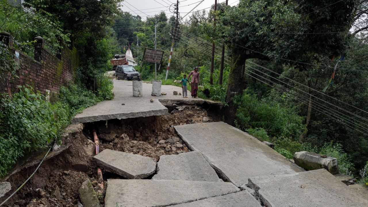 A woman and child look at a caved-in segment of a road damaged by heavy rain in Dharmsala, Himachal Pradesh state, India, on August 21, 2022.