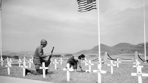An American corporal watches as a 9-year-old Korean girl places a bouquet of white roses on the grave of one of his fallen comrades at a UN memorial near Busan, South Korea, in 1951.