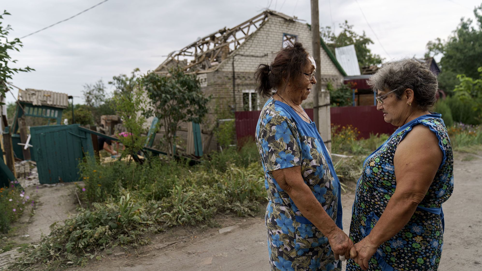 Valentyna Kondratieva, 75, left, is comforted by a neighbor as they stand outside her damaged home, in Kramatorsk, Ukraine, on August 13, after a rocket attack.