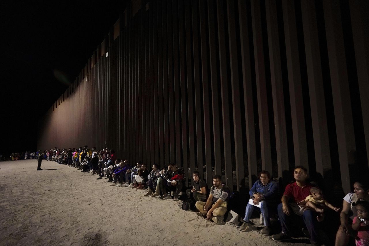 Migrants wait along a border wall in Yuma, Arizona, after crossing from Mexico on Tuesday, August 23.