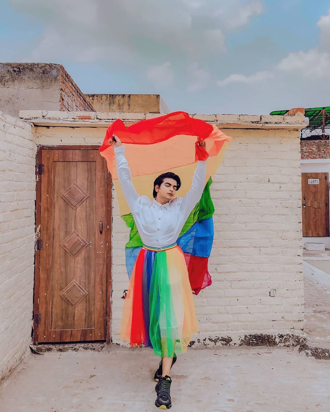 Blogger Shivam Bhardwaj of @theguyinaskirt poses wearing a rainbow skirt.