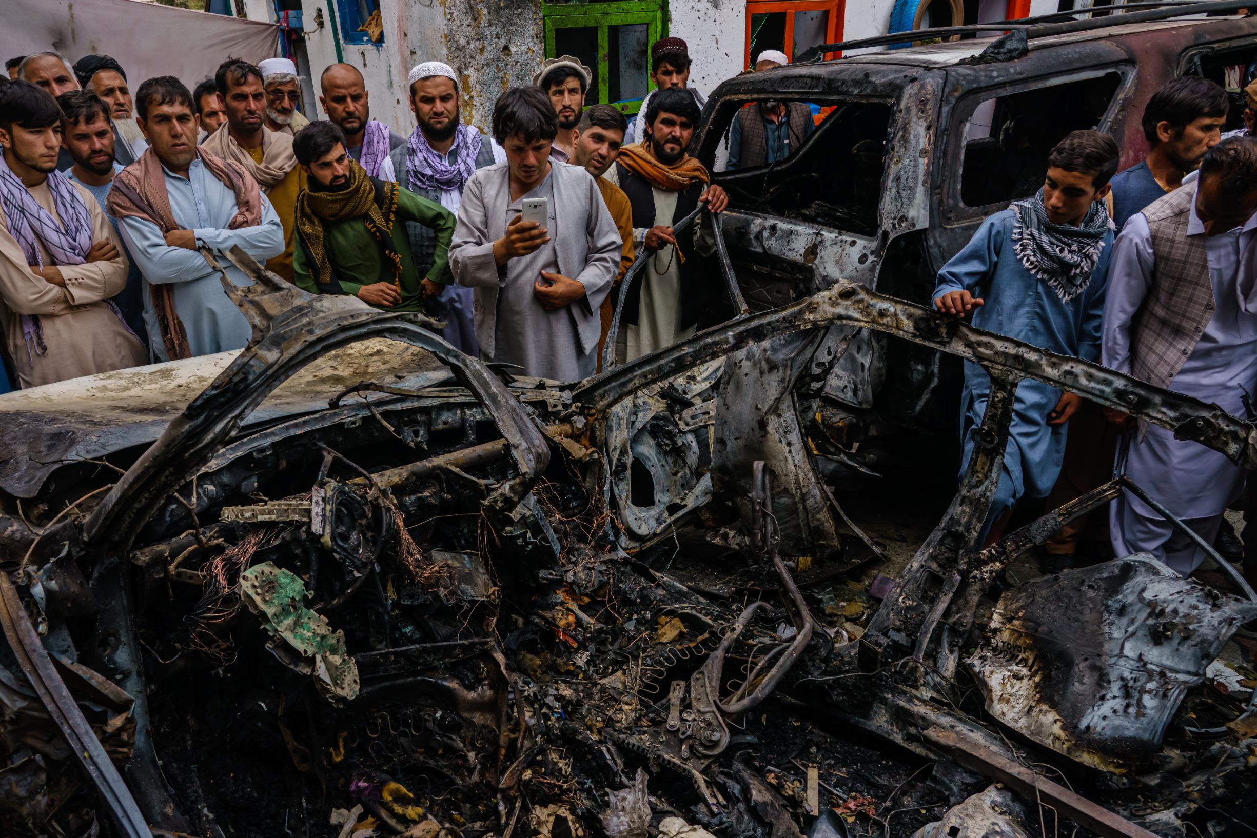 People gather around the incinerated husk of a vehicle that was hit by a US drone strike in Kabul in August 2021.