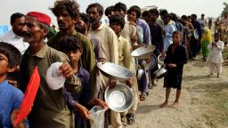Flood affected people stand in a long line with utensils to get food distributed by Pakistani Army troops in a flood-hit area in Rajanpur, district of Punjab, Pakistan, Saturday, Aug. 27, 2022. Officials say flash floods triggered by heavy monsoon rains across much of Pakistan have killed nearly 1,000 people and displaced thousands more since mid-June. (AP Photo/Asim Tanveer)