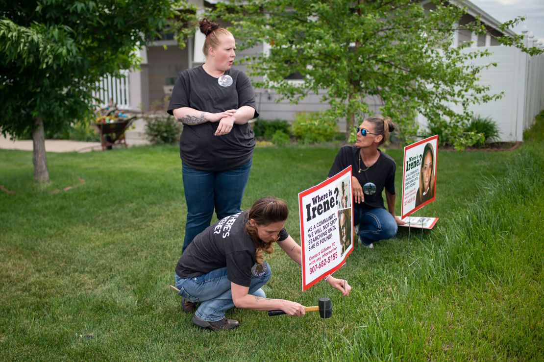 Lacey Ayers talks to Stacy Koester, left, and Melissa Bloxom as they place signs with an image of Irene Gakwa in a yard in Gillette, Wyoming. Gakwa lived with her boyfriend next door. 