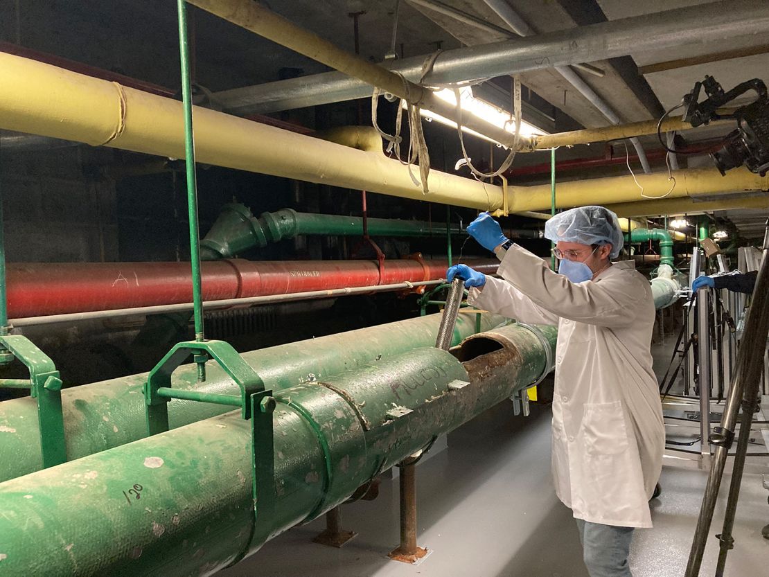 Queens College Research Assistant Justin Silbiger collects a wastewater sample from a sewage pipe in the basement of NYC Health + Hospitals/Elmhurst. 