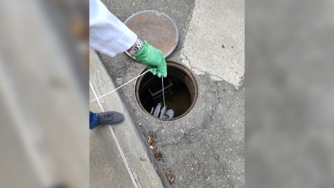 Queens College Research Assistant Sherin Kannoly collects a wastewater sample from a manhole on the grounds of NYC Health + Hospitals/Queens.