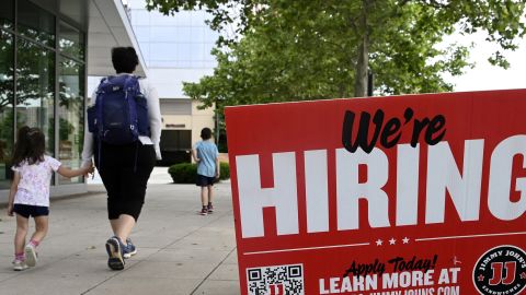People walk past a "now hiring" sign posted outside of a restaurant in Arlington, Virginia.