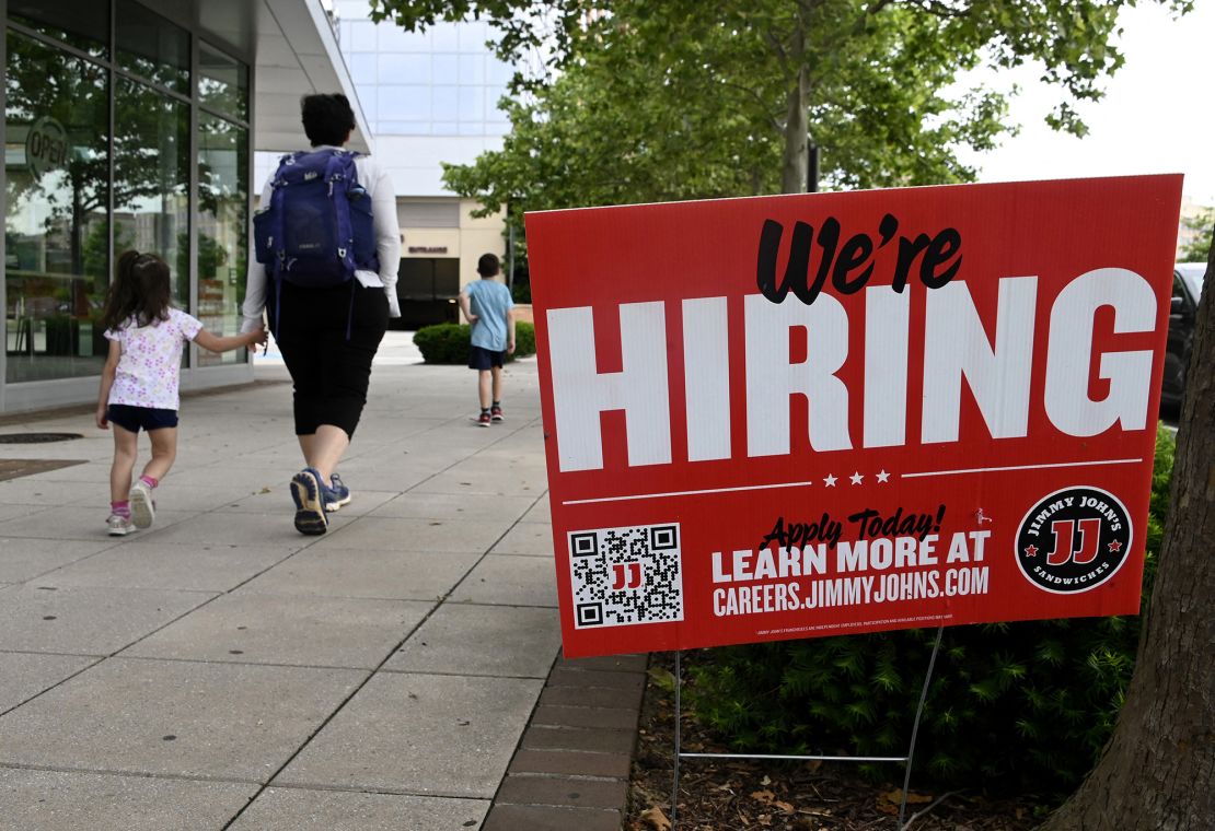 People walk past a "now hiring" sign posted outside of a restaurant in Arlington, Virginia. 