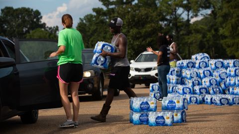 Quad Johnson, center, carries packages of bottled water Wednesday to cars at a water distribution site at Grove Park Community Center in Jackson, Mississippi.