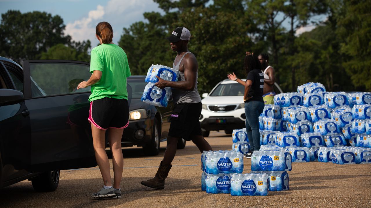 Quad Johnson, center, 24, from Jackson, carries packages of bottle water to cars at a water distribution site at Grove Park Community Center in Jackson, Mississippi, on August 31, 2022.