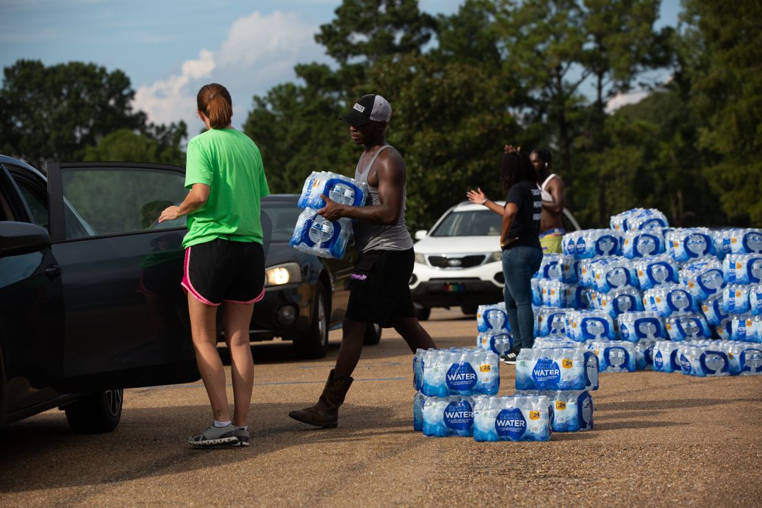 Quad Johnson, center, carries packages of bottled water Wednesday to cars at a water distribution site at Grove Park Community Center in Jackson, Mississippi.