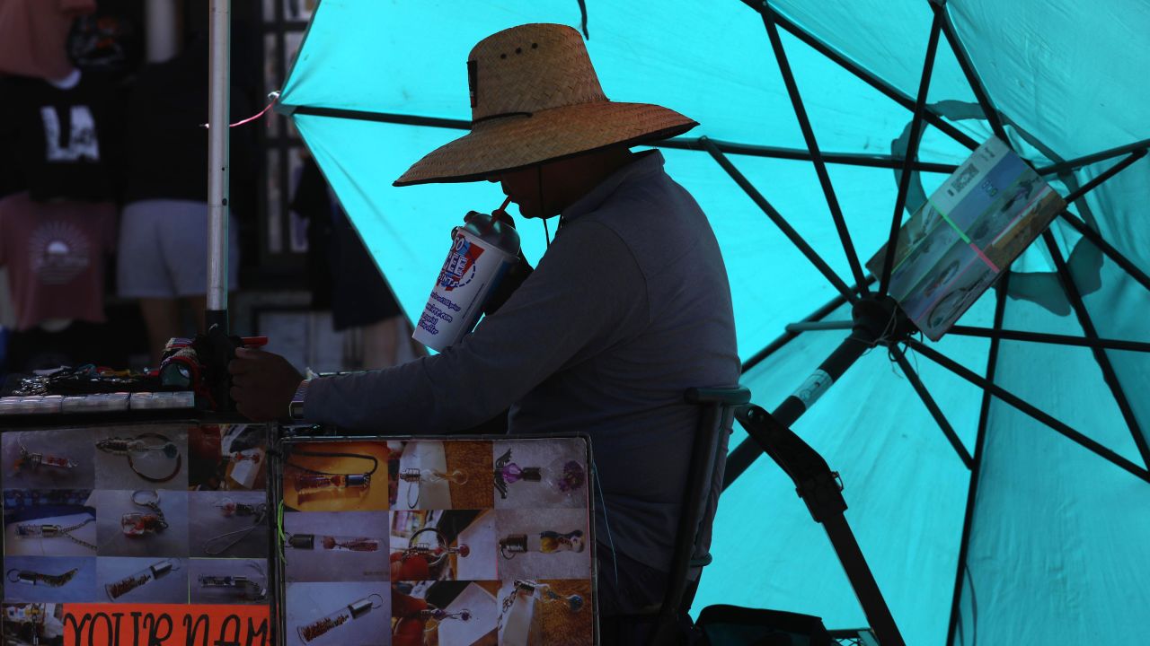 Miguel Ángel quenches his thirst under the hot sun while waiting for customers at Your Name On A Grain Of Rice on the first day of a heatwave on the Santa Monica Pier on August 31, 2022.