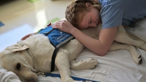 Lilly Downs, an 18-year-old who has been in and out of the hospital with long Covid, pets facility dog Posey at Denver's Rocky Mountain Hospital for Children on Tuesday, August 30. 