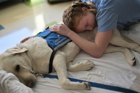 Lilly Downs, an 18-year-old who has been in and out of the hospital with long Covid, pets facility dog Posey at Denver's Rocky Mountain Hospital for Children on Tuesday, August 30. 