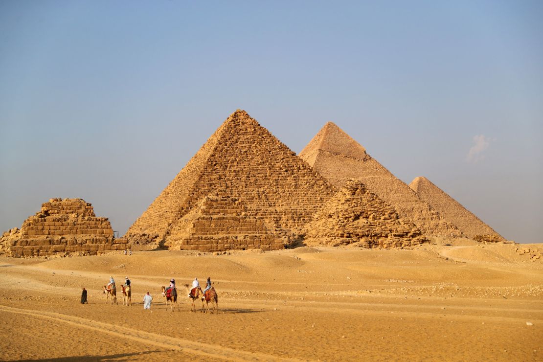 Tourists ride camels to view the Giza Pyramids in Egypt on October 21, 2021. 