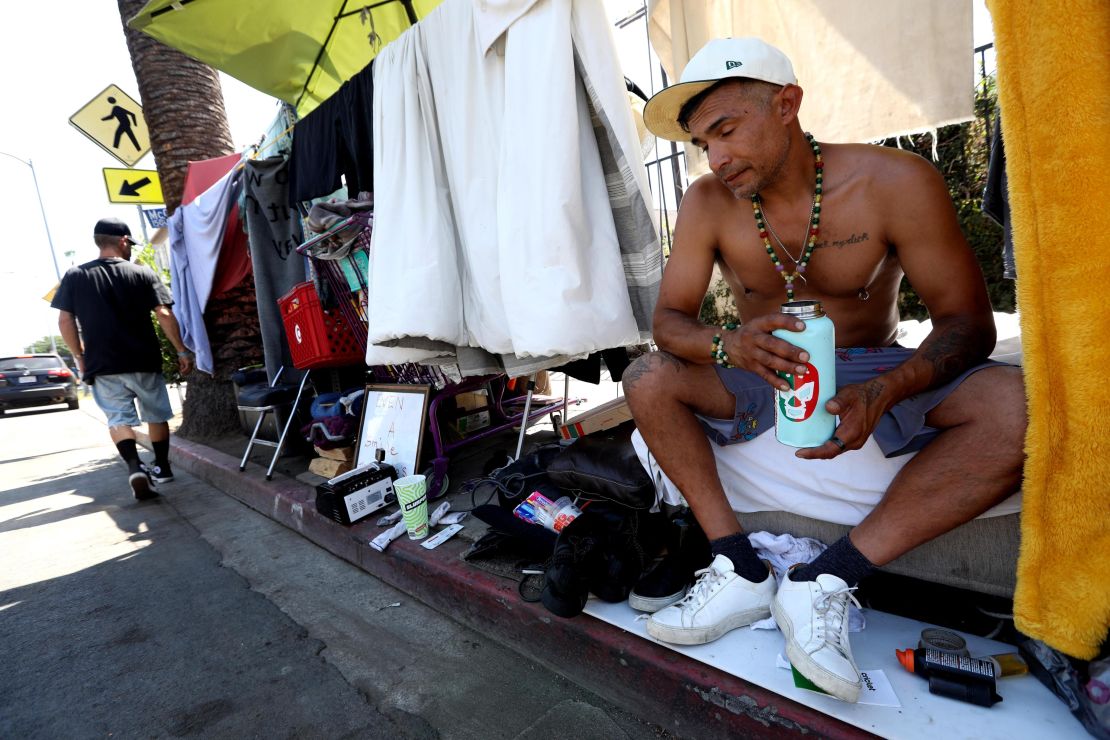 Vasilis Sakellaridis, holding a container of Gatorade, tries to stay cool within his homeless encampment along Selma Avenue during a heat wave in Hollywood Saturday.
