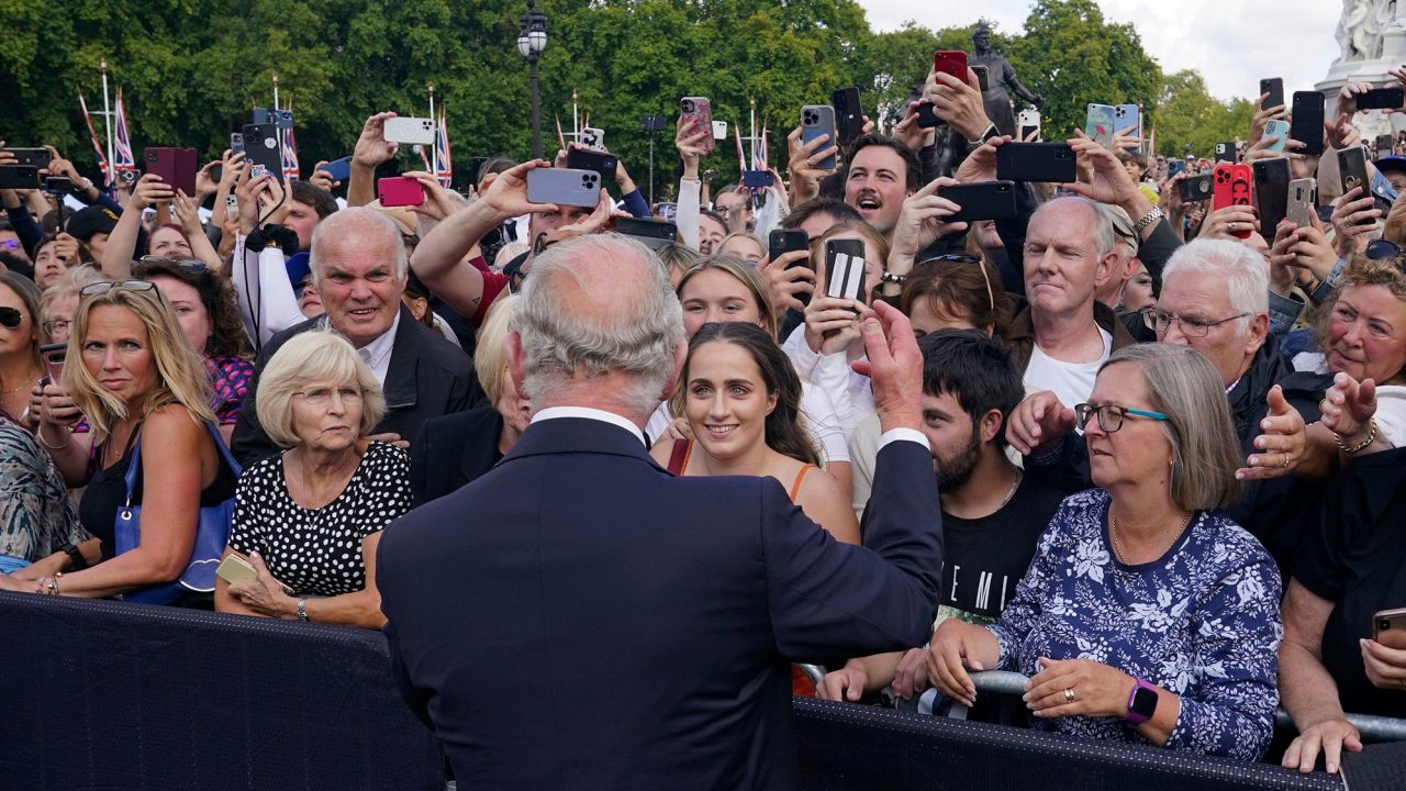 Britain's King Charles III, back to camera, greets well-wishers at Buckingham Palace.