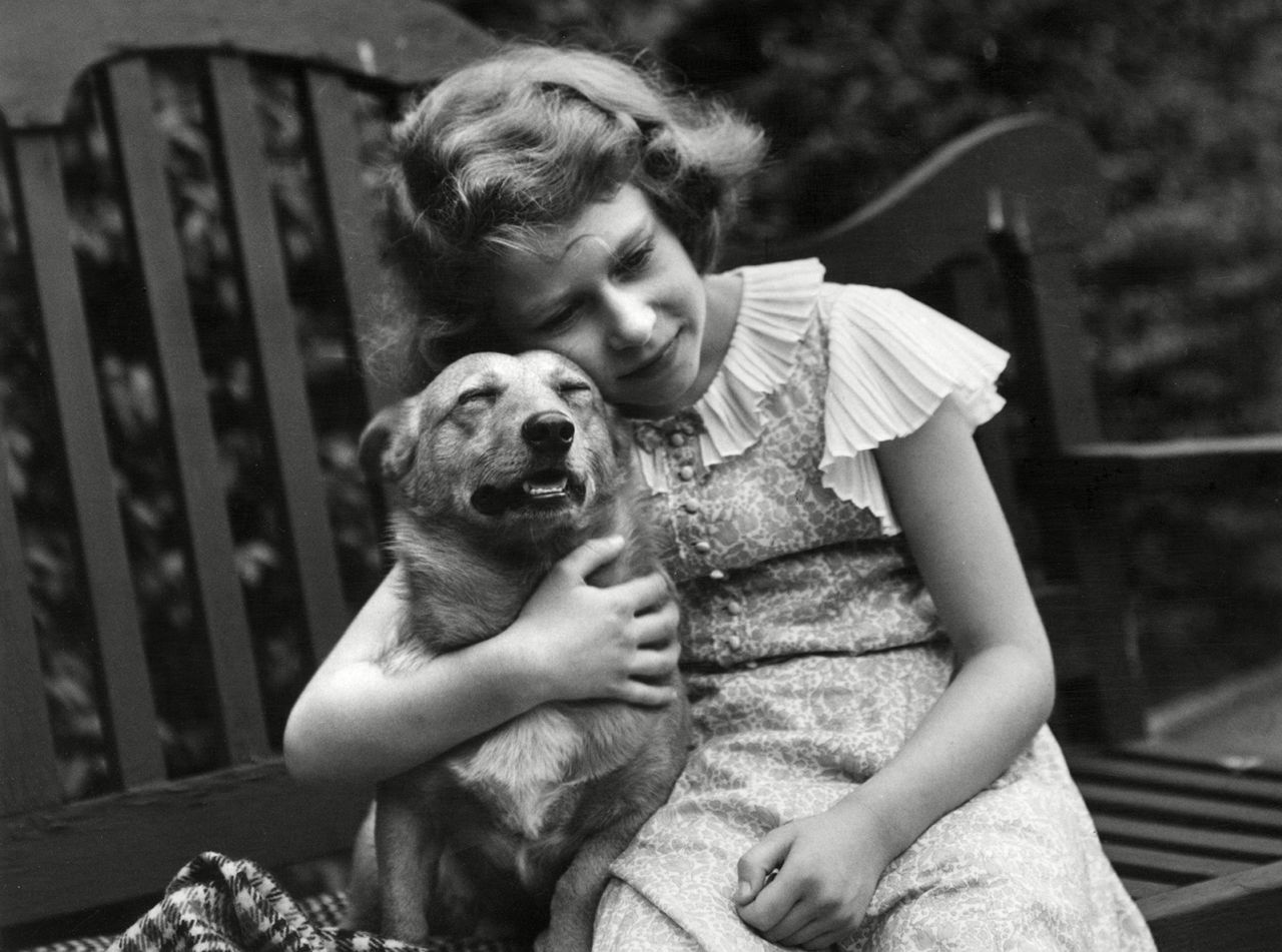 A young Elizabeth, then a princess, gives a corgi a comforting hug at her home in London in 1936.
