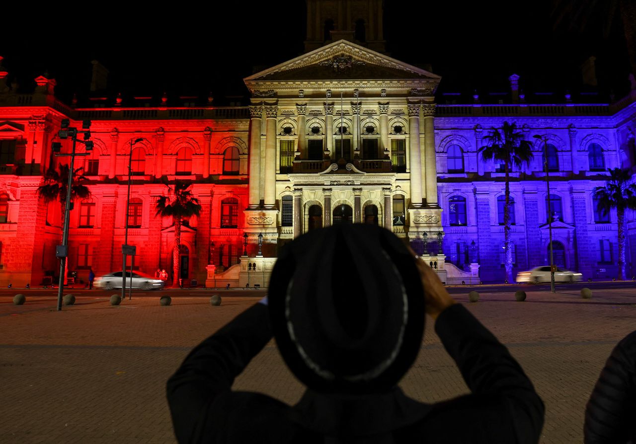 A man takes a picture of City Hall in Cape Town, South Africa, which is illuminated in the colors of the Union Jack flag.