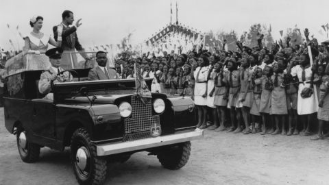 Königin Elizabeth II. und Prinz Philip winken am 15. Februar 1956 bei einer Kundgebung auf einer Pferderennbahn in Ibadan, Nigeria, einer Menge Schulkinder zu.