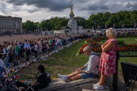 People stand in line to lay flowers and pay their respects to the Queen in front of Buckingham Palace.