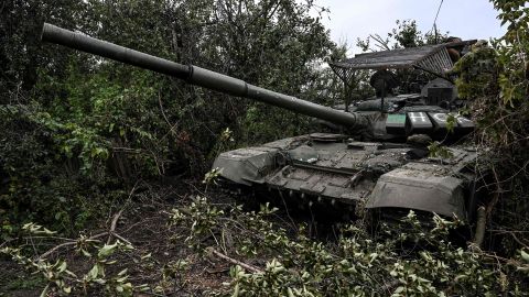 रविवार को यूक्रेन के इज़ियम के बाहरी इलाके में एक गाँव में एक परित्यक्त रूसी टैंक वनस्पति में बैठता है।