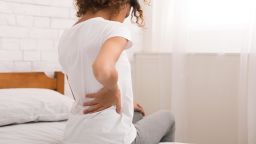 African-american woman having back pain after sleep, sitting on bed