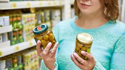 Woman chooses canned olives in the grocery store